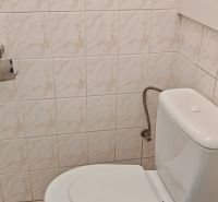 A bathroom in a 2-room apartment with a toilet, white tiles, and light flooring.