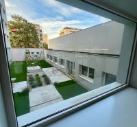 A view from the window of a one-room apartment onto an inner courtyard with greenery and benches.