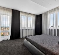 A bedroom in a 4-room apartment with dark curtains and a view of the city.