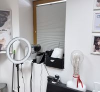 Hair salon with a ring light, mannequin head, and decorative pictures on the walls.