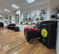 Commercial space with wood-patterned flooring, hairdressing chairs, and products on the wall.