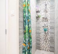 A shower corner with tiles and a colorful curtain in a 2-room apartment.