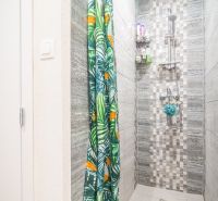A shower corner in a 2-room apartment with a colorful curtain and wall tiles.
