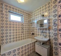 A bathroom in a family house with patterned tiles, a bathtub, and a sink with a mirror.
