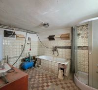 A bathroom in a family house with a bathtub and a shower, older tiles and flooring.