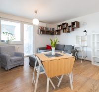 Living room in a two-room apartment with a wooden decor floor, a sofa, and shelves.
