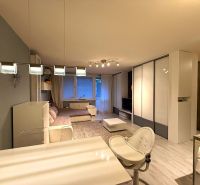 Interior of a 2-room apartment with a wooden decor floor, a large sofa, and a dining table.