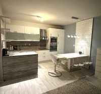 A kitchen area in a two-room apartment with a wood-patterned floor, a dining table, and a kitchen unit.