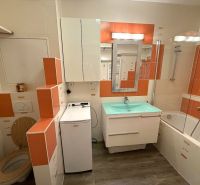 Bathroom in a 2-room apartment with a bathtub, washing machine, and orange tiles.