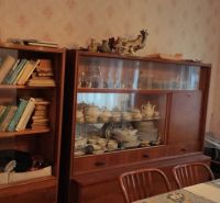 Dining room in a family house with a showcase full of porcelain and books on wooden shelves.