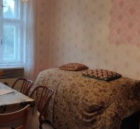 A room in a family house with floral wallpaper, a table, and a bed by the window.