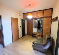 A hallway with a wooden decor floor in a 3-room apartment with lighting and a chair.
