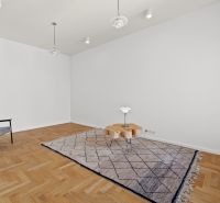 A spacious room with a wooden decor floor in a 4-room apartment, a rug, and a chair.