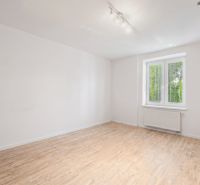 White room in a family house with a wood-patterned floor and a window.