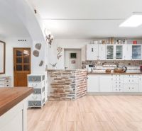 A kitchen in a family house with white cabinets, brick elements, and a wooden-patterned floor.