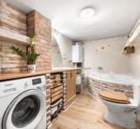 A bathroom in a family house with a bathtub, a washing machine, and a wooden decor floor.