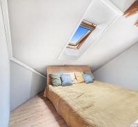 Attic room in a family house with a bed, skylight, and wooden decor flooring.