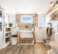 A bathroom in a family house with a brick wall, a wooden decor floor, and rustic decorations.
