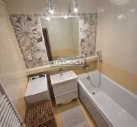 Bathroom in a 2-room apartment with a bathtub, washing machine, and tiles.