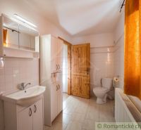 A bathroom in a family house with a shower, sink, and toilet, white tiles, orange curtain.