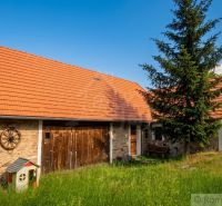 A family house in Budiná with a gable roof and stone walls, surrounded by greenery.