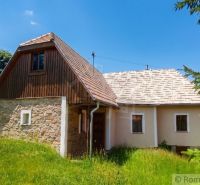 A family house in Budiná with a sloped roof and stone walls surrounded by greenery.