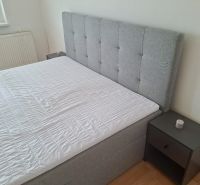 Gray bed with upholstered headboard and nightstand in a 3-room apartment.