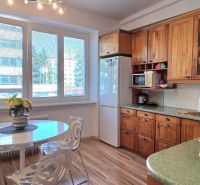 A kitchen in a 2-room apartment with a light table, wooden cabinets, and a floor with a wooden decor.