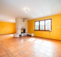 A spacious room with a fireplace and large windows in a family house, tiles on the floor.