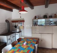 A dining room with a tiled stove, an old sideboard, and a colorful tablecloth on the table.
