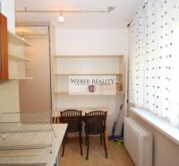 A kitchen in a one-room apartment with shelves, a table, and two chairs.