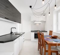 A kitchen in a 2-room apartment with white cabinets, a black countertop, and a dining table.