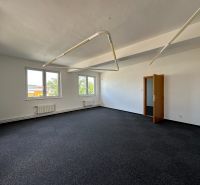 A spacious office with carpeted flooring and white walls, equipped with pendant lighting.