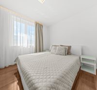 A bedroom with a large bed, white walls, and a wood-patterned floor in a family house.