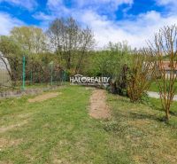 Gardens in Považská Bystrica with a grassy area, trees, and a greenhouse under a blue sky.