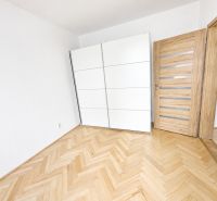 A room in a two-room apartment with a wood-patterned floor and a white wardrobe.
