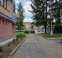 The exterior of an apartment building in Banská Bystrica with an adjacent parking lot and greenery.