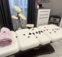 Massage table with towel, flower petals, and lava stones in commercial premises.