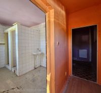 A bathroom in a cabin with tiles and a sink, next to an orange hallway.