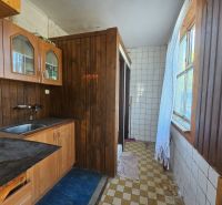 Interior of a cabin with a wooden kitchen unit and a tiled wall.