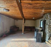 A cottage with a stone fireplace and a wooden ceiling, tiled floor, sofas.