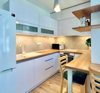 A kitchen in a 2-room apartment with a wooden decor floor and white furniture.