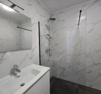 Bathroom in a family house with marble tiles, a shower, and a sink with a large mirror.