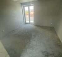 A vacant room in a three-room apartment with a concrete floor and plastered walls.