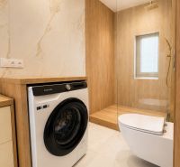 Bathroom in a 3-room apartment with a washing machine, shower cabin, and toilet, floor with wooden decor.