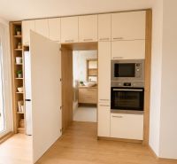 A kitchen with white cabinets and appliances, a floor with a wood decor, a 3-room apartment.