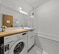 A bathroom with a washing machine, bathtub, and sink in a 3-room apartment.