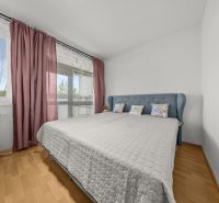 A bedroom with a large bed, a wooden-patterned floor, and pink curtains in a 3-room apartment.