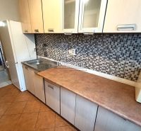 A kitchen of a three-room apartment with mosaic tiles and a wooden decor floor.