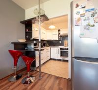 A kitchen in a 2-room apartment with bar stools and a wooden decor floor.